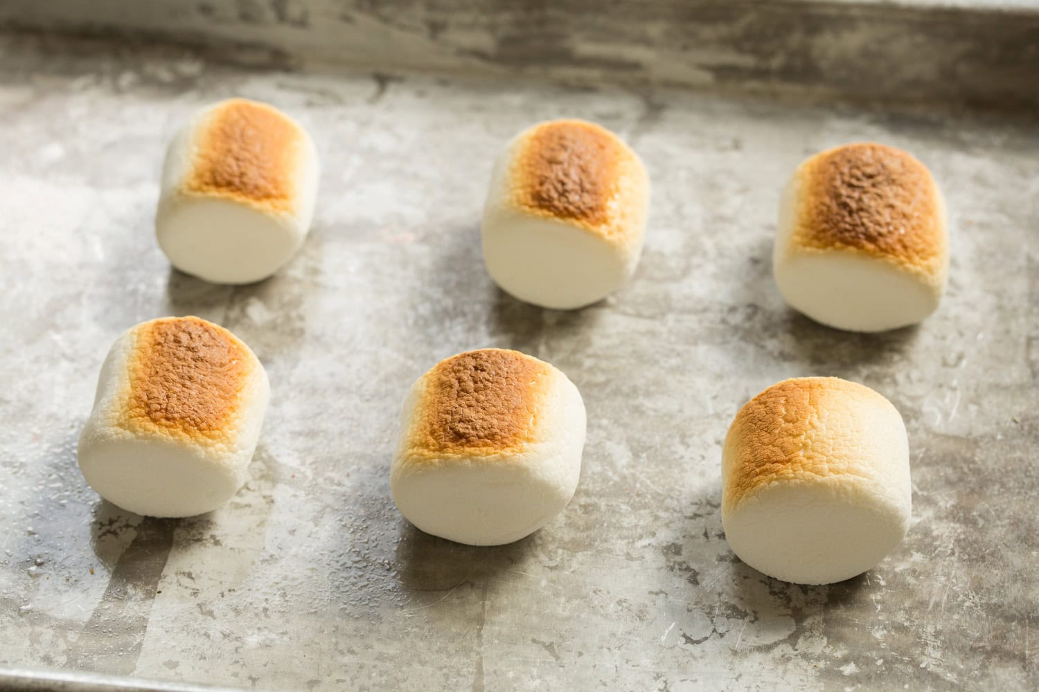 Six toasted marshmallows on baking sheet after broiling on one side.