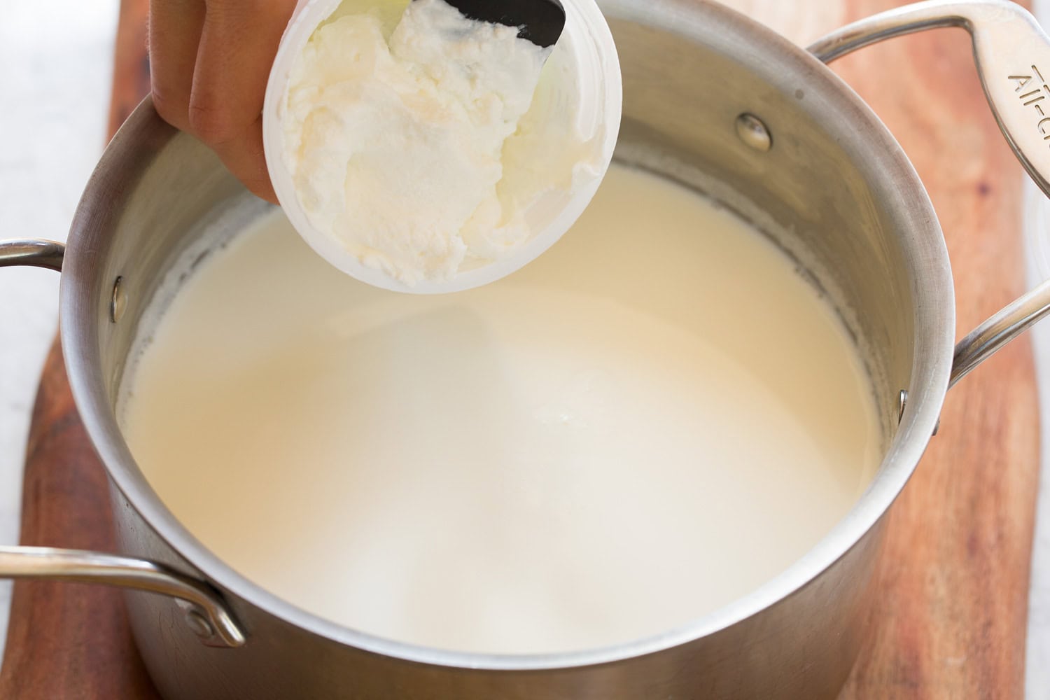 Adding greek yogurt to milk in pot.